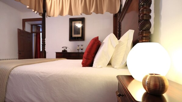 A neatly made bed with a wooden headboard, a bedside table with a lamp, and a red and white pillow.