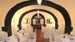 Un ristorante con tavoli apparecchiati per la cena, caratterizzato da un arco centrale e un dipinto sulla parete di fondo.