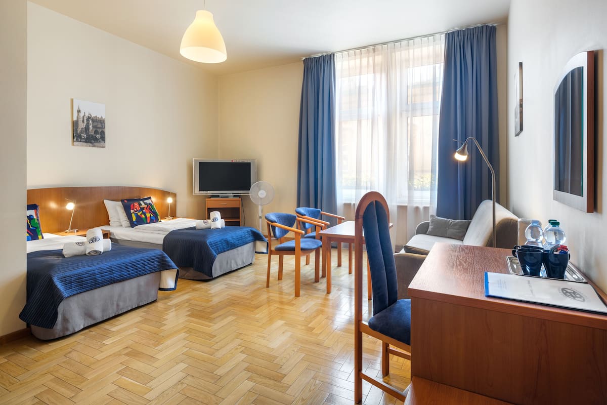 A hotel room with two beds, a desk, a chair, a TV, and a large window with curtains.