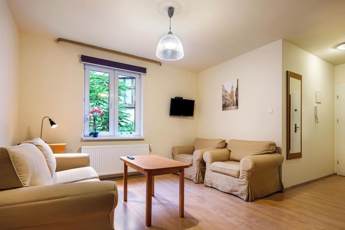 A living room with a sofa, a table, and a window with a view of greenery.