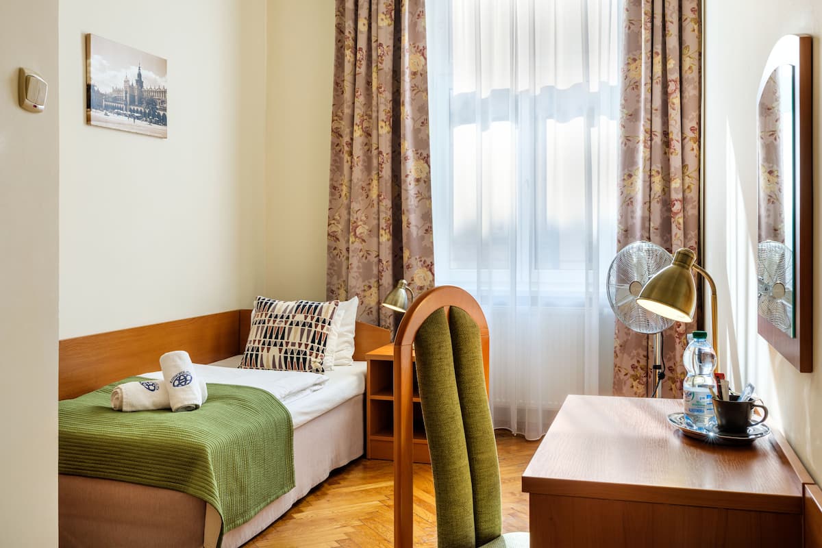 A neatly arranged bedroom with a bed, a bedside table with a lamp, a chair, and a small table with a water bottle and cup.