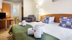 Una habitación de hotel con una cama, un escritorio con computadora, una silla, una lámpara y un cuadro en la pared.