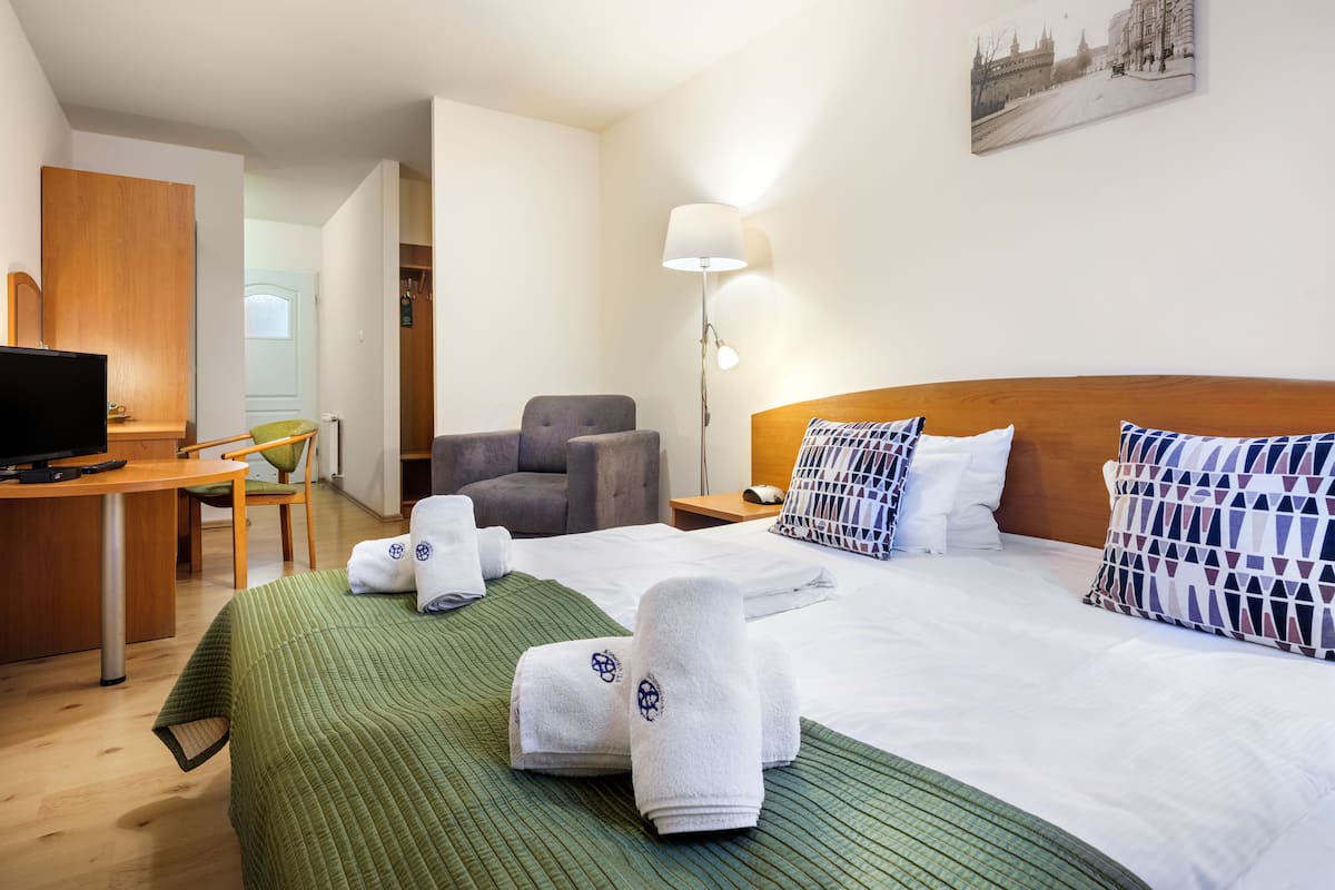 A hotel room with a bed, a desk with a computer, a chair, a lamp, and a painting on the wall.