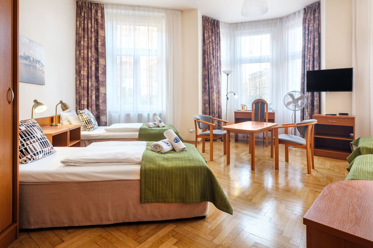 A hotel room with two beds, a desk, a chair, a television, and a large window with curtains.