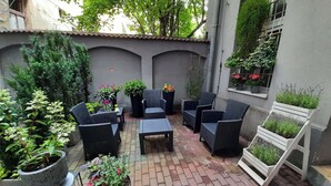 Un patio con mobiliario de mimbre, plantas en macetas y piso de ladrillo.