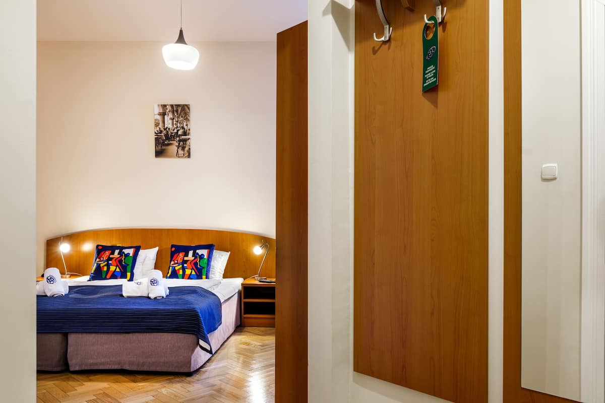 A hotel room with a wooden headboard, a bed with colorful pillows, a bedside table with a lamp, and a wooden floor.