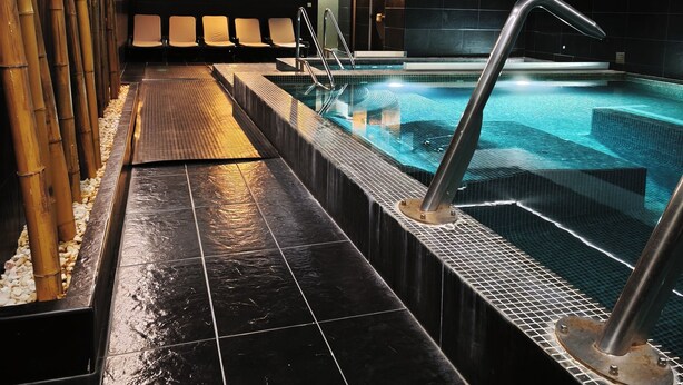 A modern indoor swimming pool with clear water, surrounded by black tiled flooring and bamboo accents. - Douro Marina Hotel & SPA (Resende)