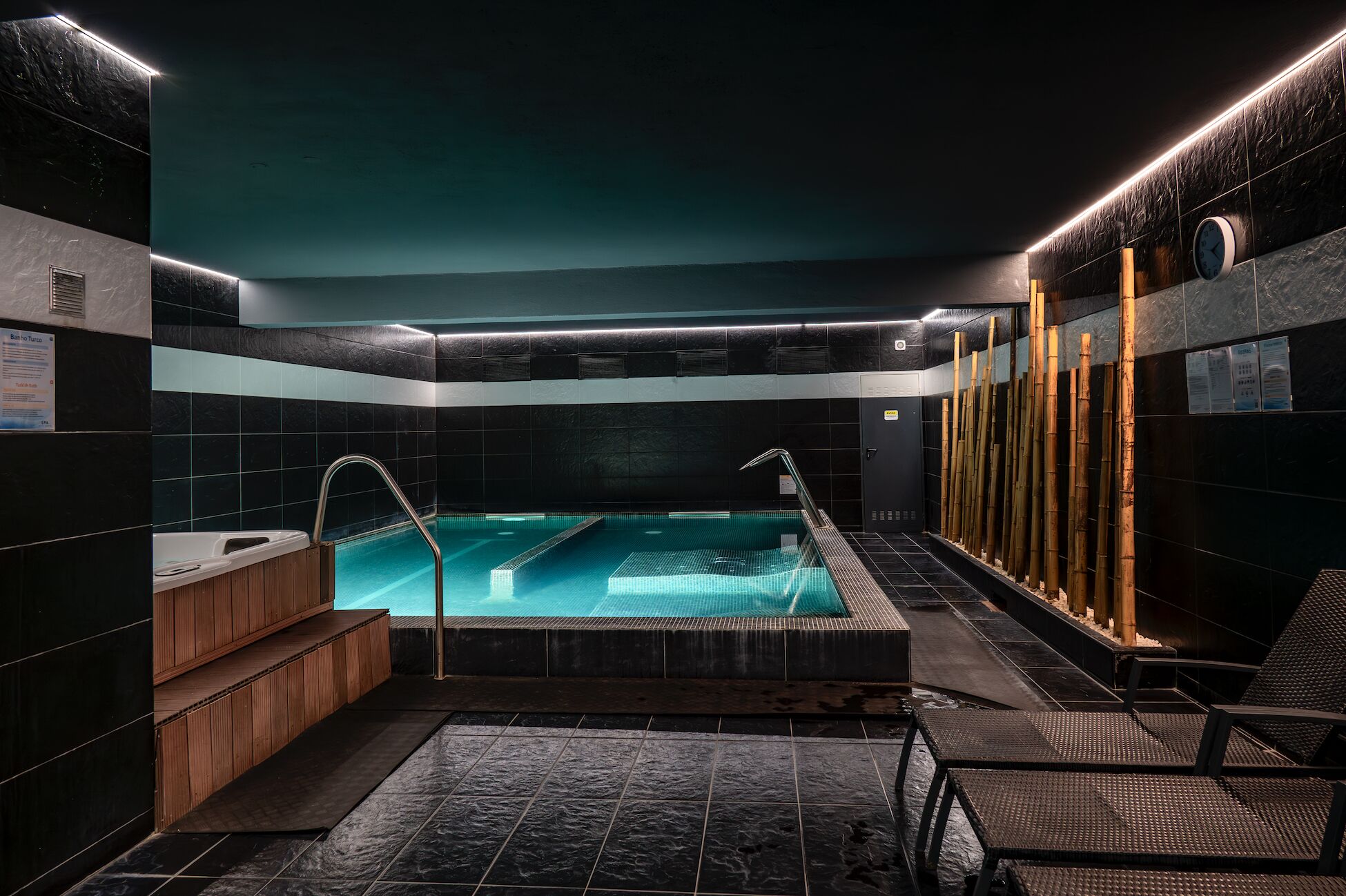 A modern indoor swimming pool with a wooden bench and a bamboo wall.