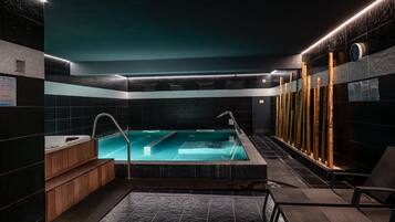 A modern indoor swimming pool with a wooden bench and a bamboo wall.