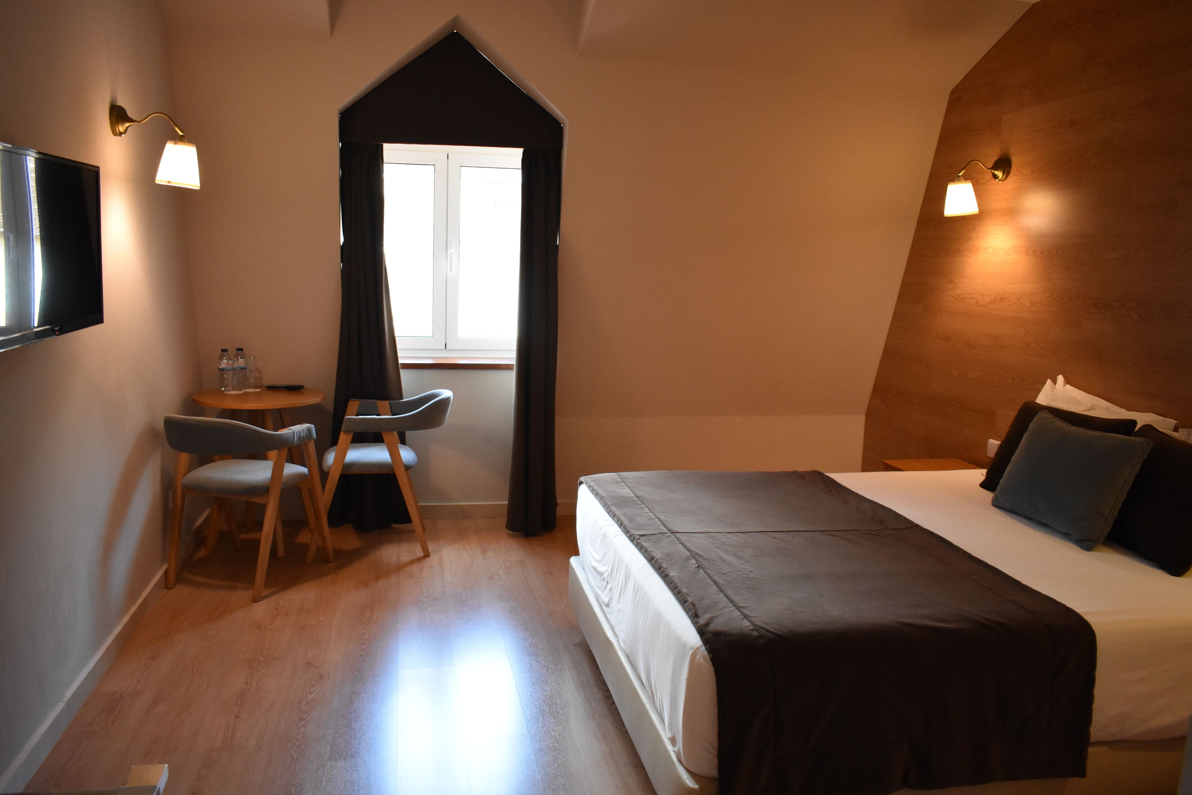 A hotel room with a bed, a desk with a chair, a TV, and a window with curtains.