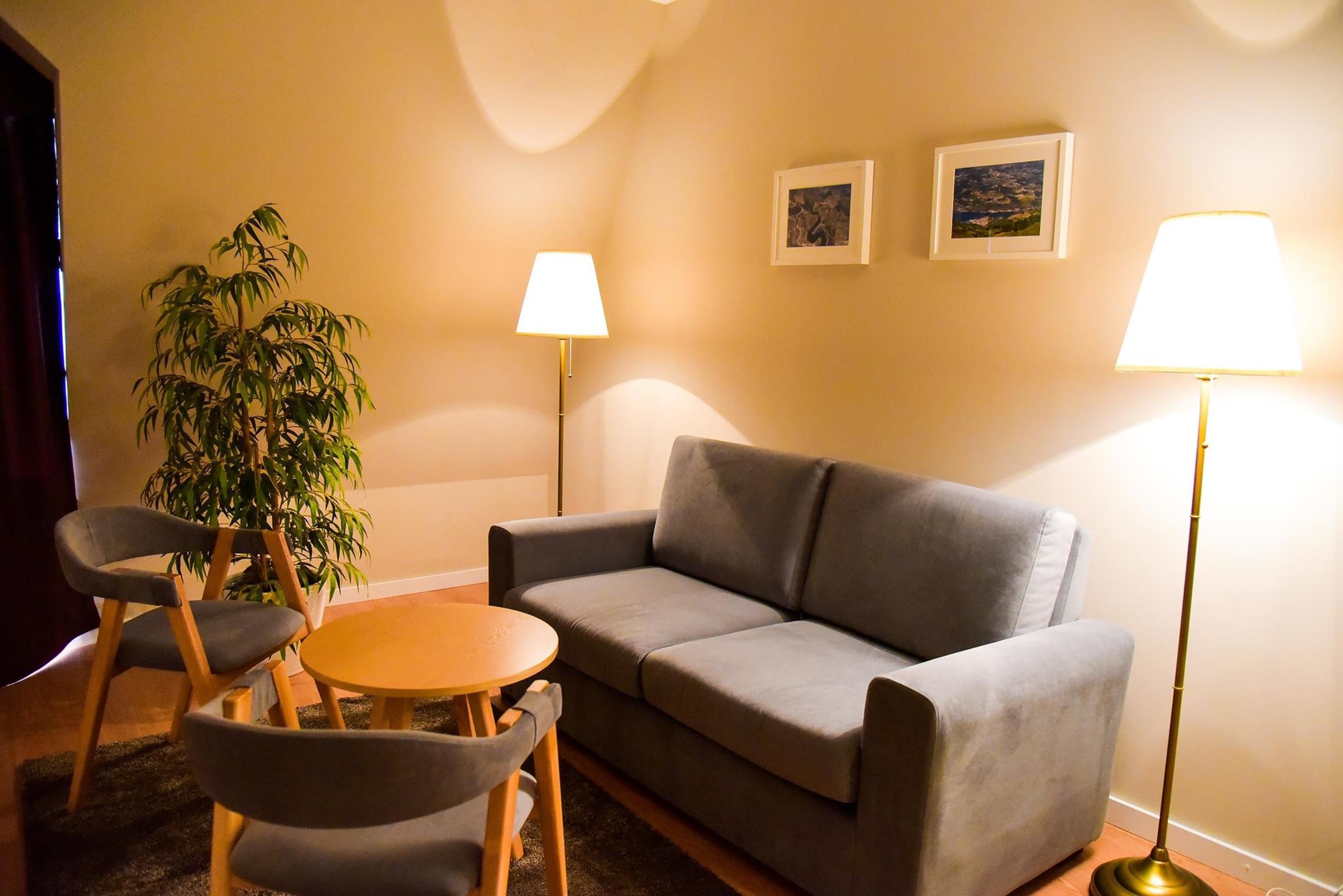 A living room with a grey sofa, two armchairs, a small round table, a floor lamp, and a potted plant.