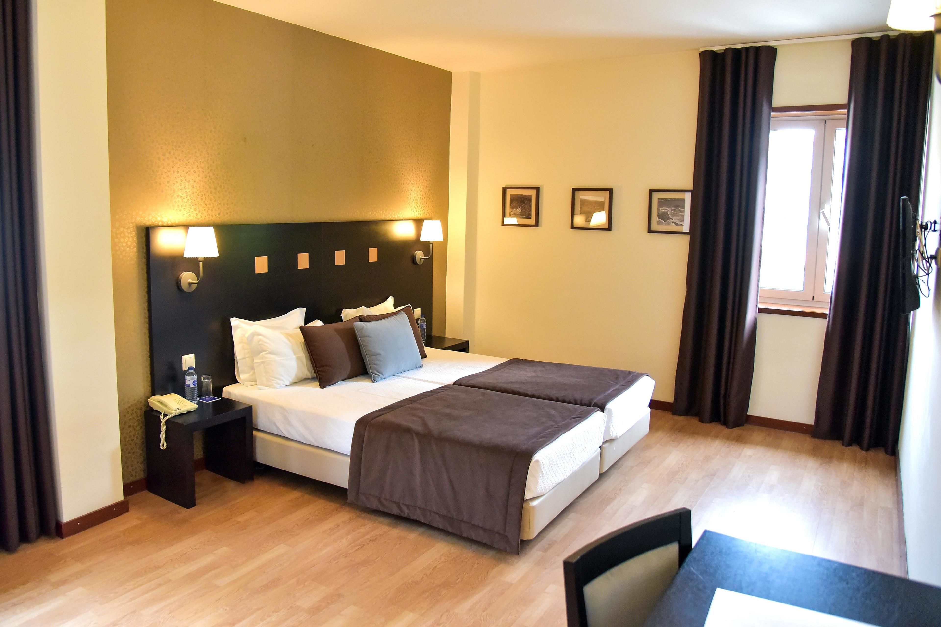 Een hotelkamer met een tweepersoonsbed, nachtkastjes, een bureau en een stoel.