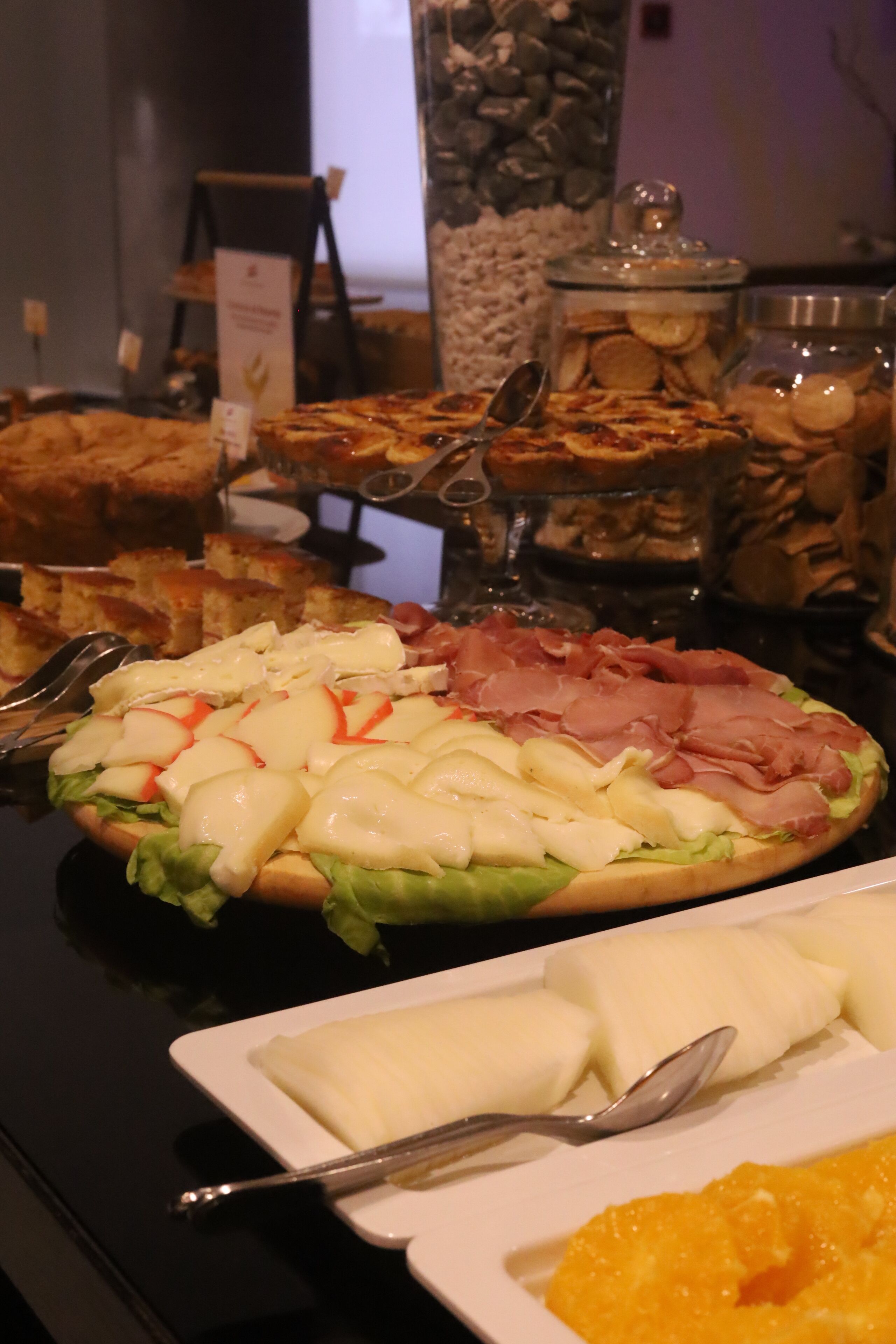 Een buffet met diverse gerechten, waaronder een salade met kaas en ham, brood en een bakje koekjes.