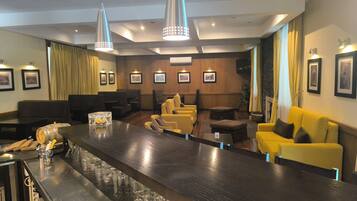 A bar area with a long counter, multiple seating options including yellow sofas and a black couch, and a television mounted on the wall.