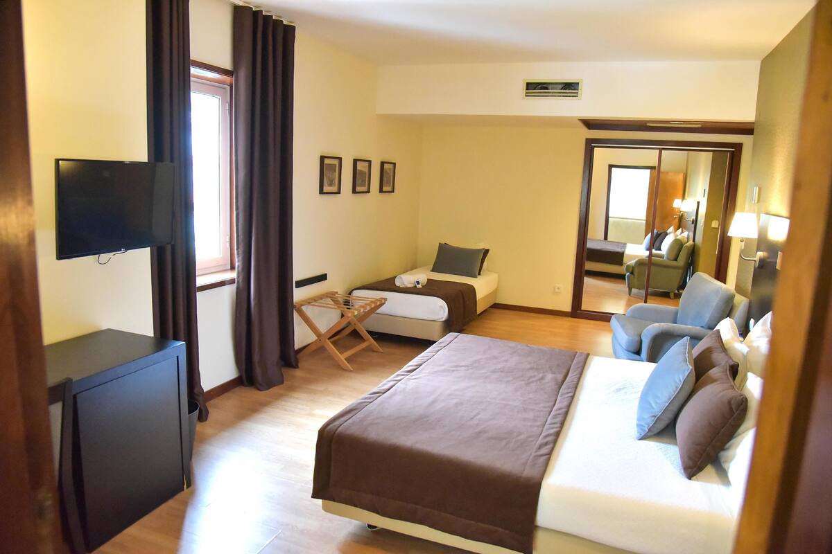 A hotel room with a bed, a desk, a chair, a TV, and a window with curtains.