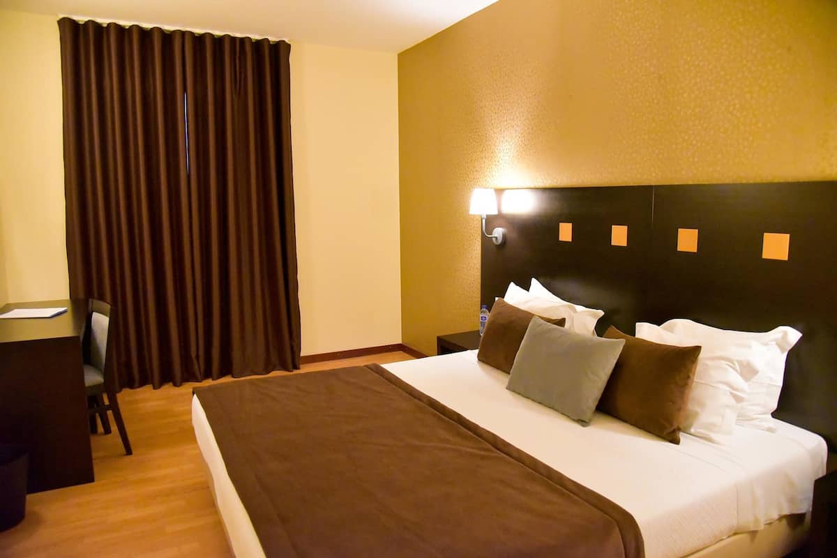A hotel room with a large bed, a desk, a chair, and a nightstand.