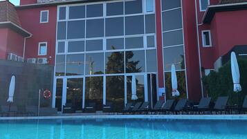 A hotel with a swimming pool, sun loungers, and a red facade.