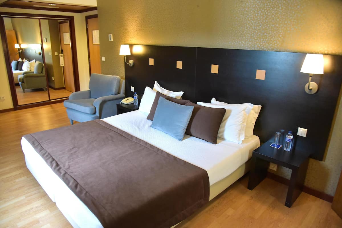 A hotel room with a large bed, a chair, a nightstand, and a mirror.