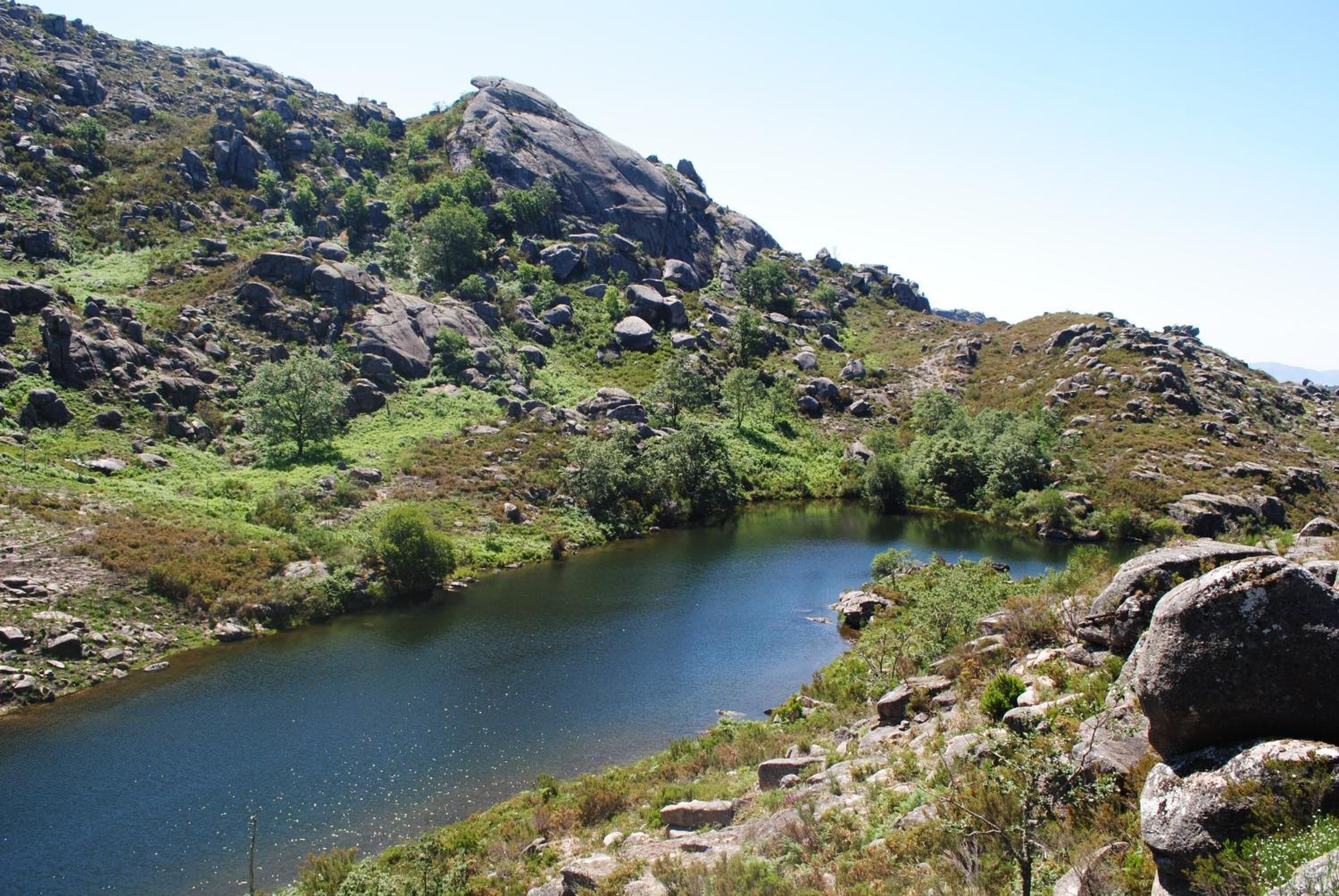 Un paysage naturel composé d’un petit lac entouré de reliefs rocheux et d’une végétation clairsemée.