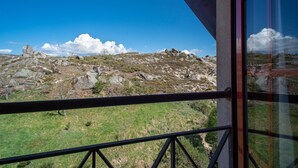 Vista desde un balcón sobre una ladera rocosa con vegetación escasa y un cielo azul despejado.