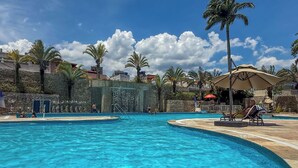 A swimming pool with clear blue water, surrounded by palm trees and a stone wall. - Wyndham Rio Barra - Oficial (Rio de Janeiro)