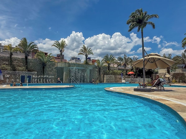 A swimming pool with clear blue water, surrounded by palm trees and a stone wall. - Wyndham Rio Barra (Rio de Janeiro)