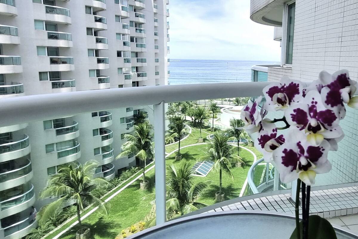Ein Balkon mit Blick auf ein modernes Gebäude, Palmen und eine Blume.