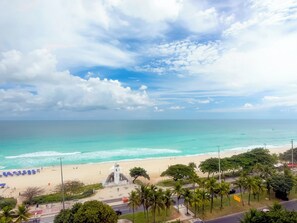 A beach view with a clear sky, a sandy shore, and a few people. - Wyndham Rio Barra - Oficial (Rio de Janeiro)