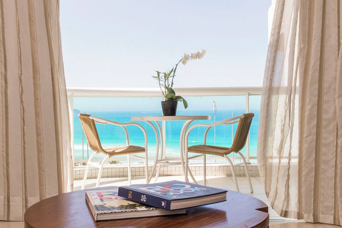 Ein Balkon mit zwei Korbstühlen, einem kleinen Tisch mit Topfpflanze und Buch sowie Blick aufs Meer.
