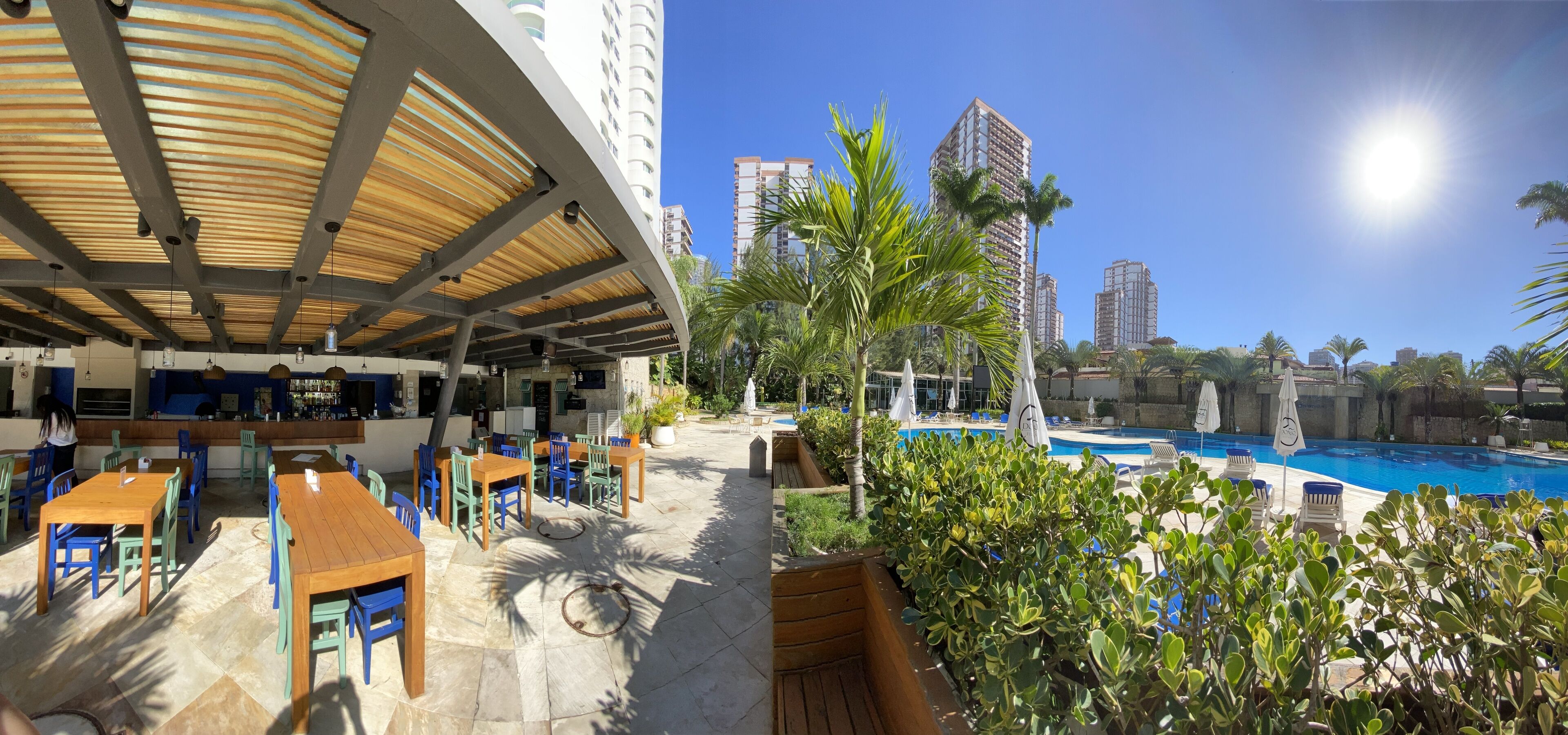 An outdoor dining area with tables and chairs, a pool, and tall buildings in the background.