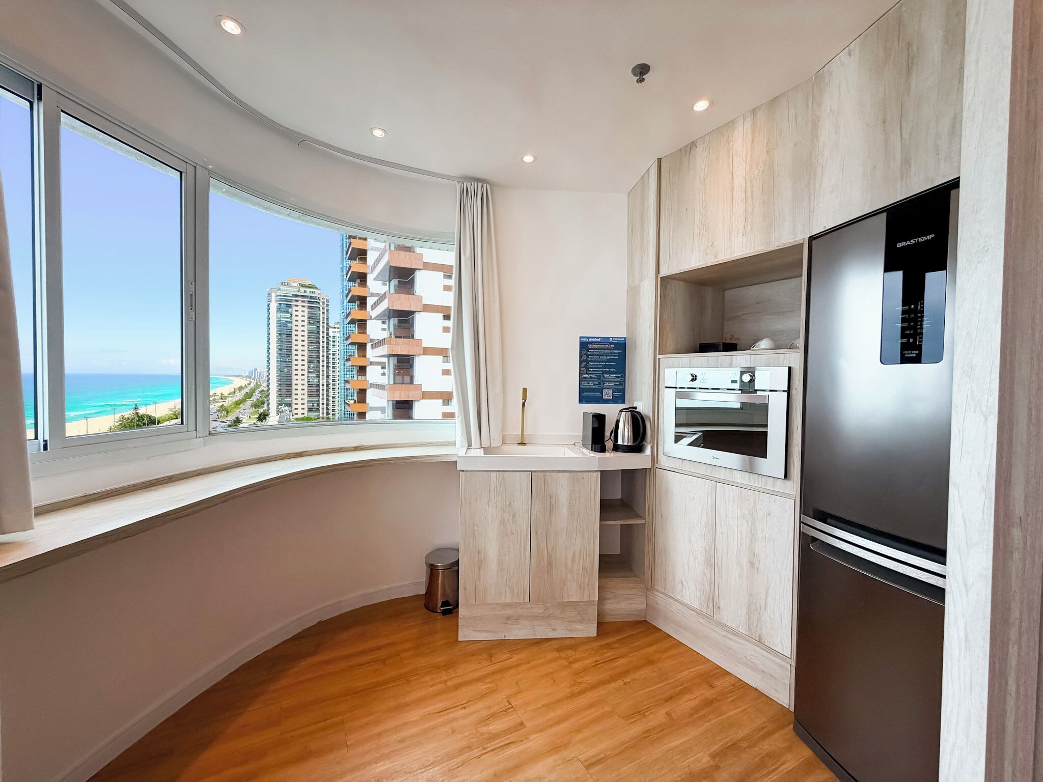 A modern kitchen with a built-in oven, a refrigerator, and a view of the beach.