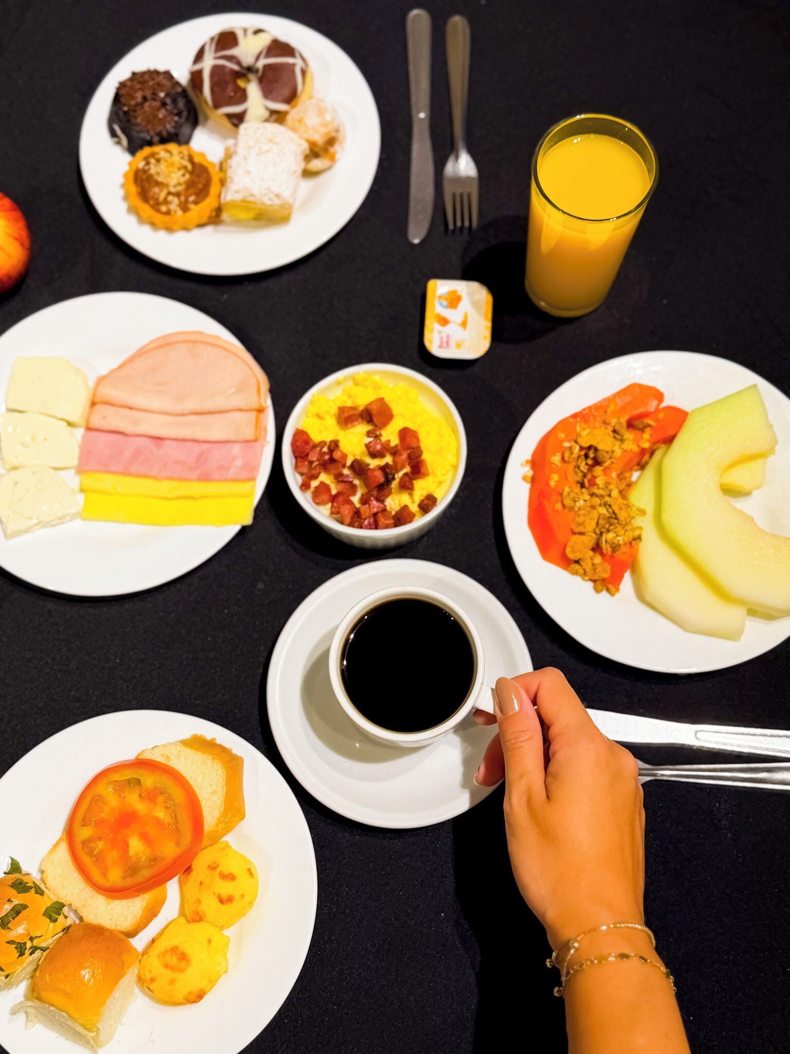 Una mesa de desayuno con diversos platos, un vaso de jugo de naranja y una taza de café.