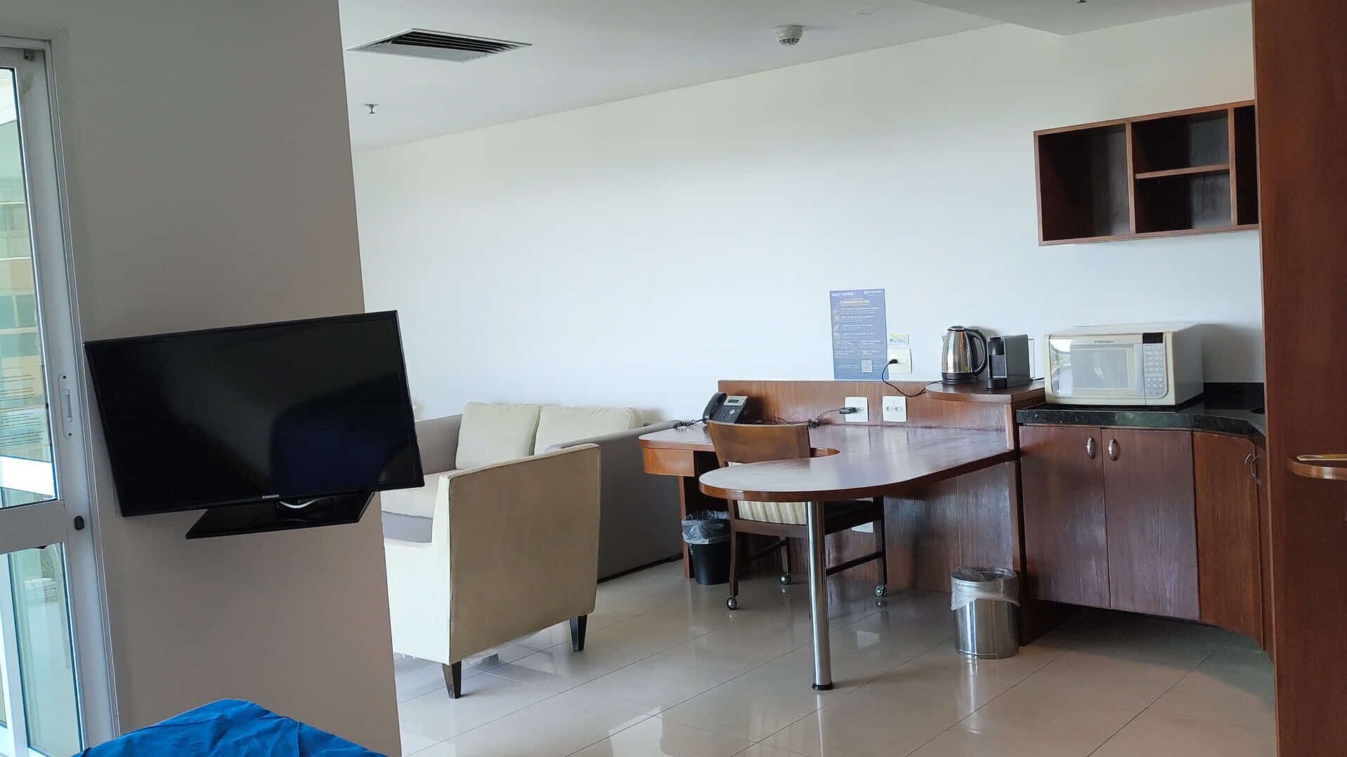 Un espacio habitable compacto con kitchenette, un televisor de pantalla plana en la pared, un sofá, una pequeña mesa de comedor y un microondas.