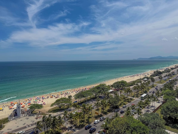 A beach with a road running parallel to it, lined with palm trees and parked cars. - Wyndham Rio Barra (Rio de Janeiro)