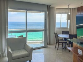 Quarto de hotel com varanda, televisão, mesa de jantar e sofá.