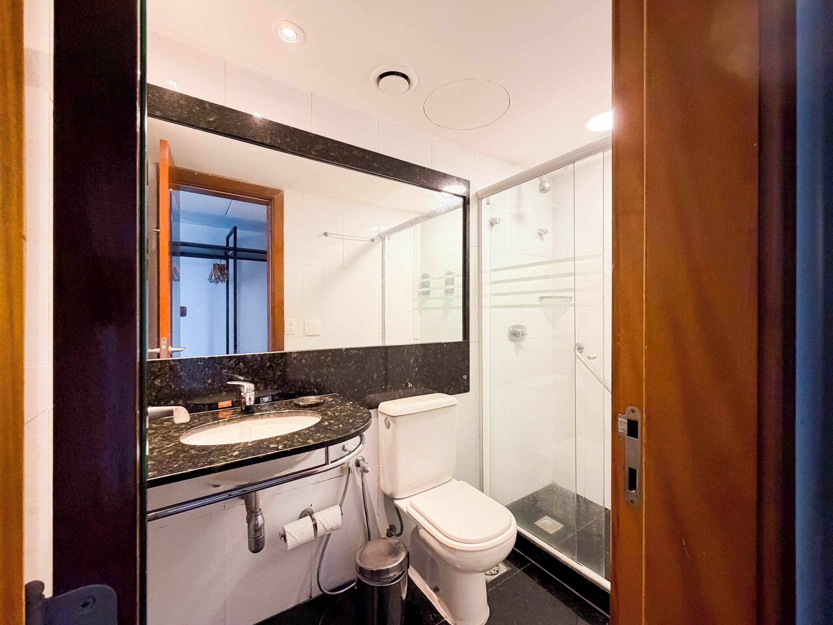 A modern bathroom with a black marble sink, white toilet, and a glass-enclosed shower.