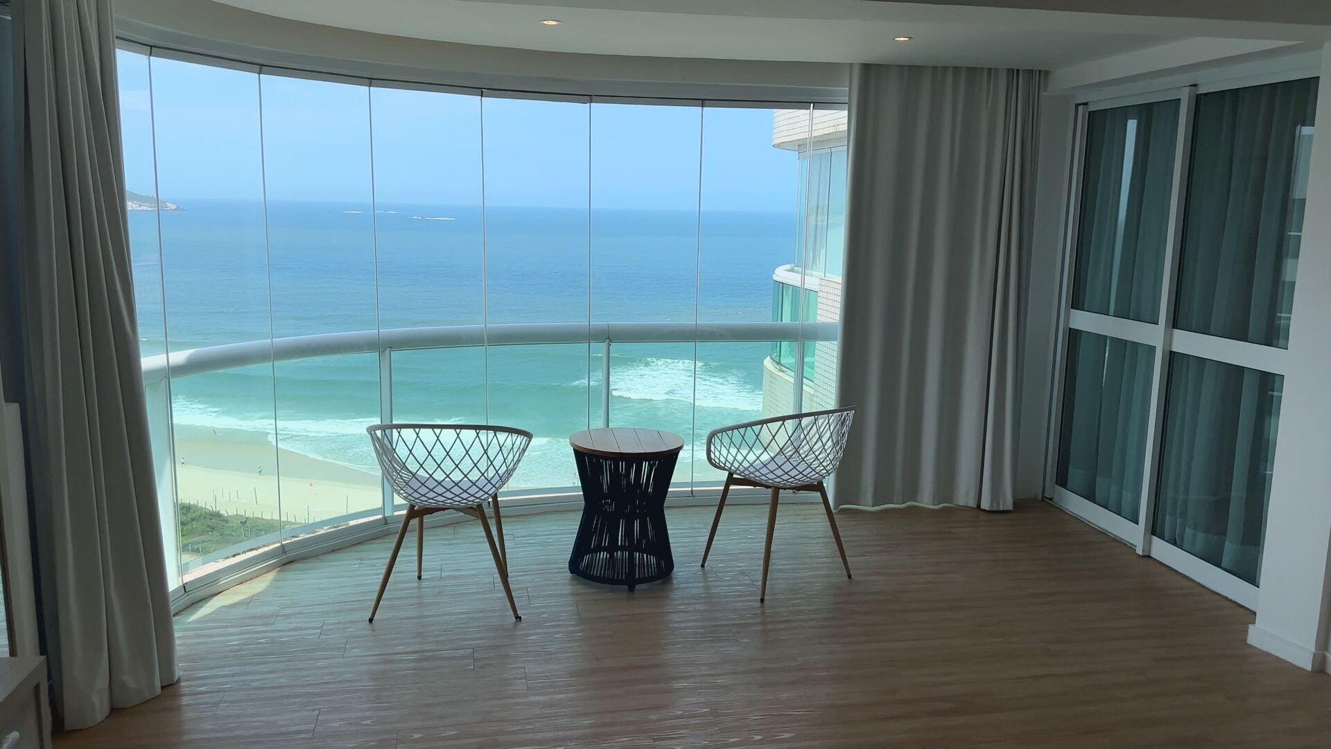 Uma varanda com vista para o oceano, duas cadeiras e uma mesa redonda.
