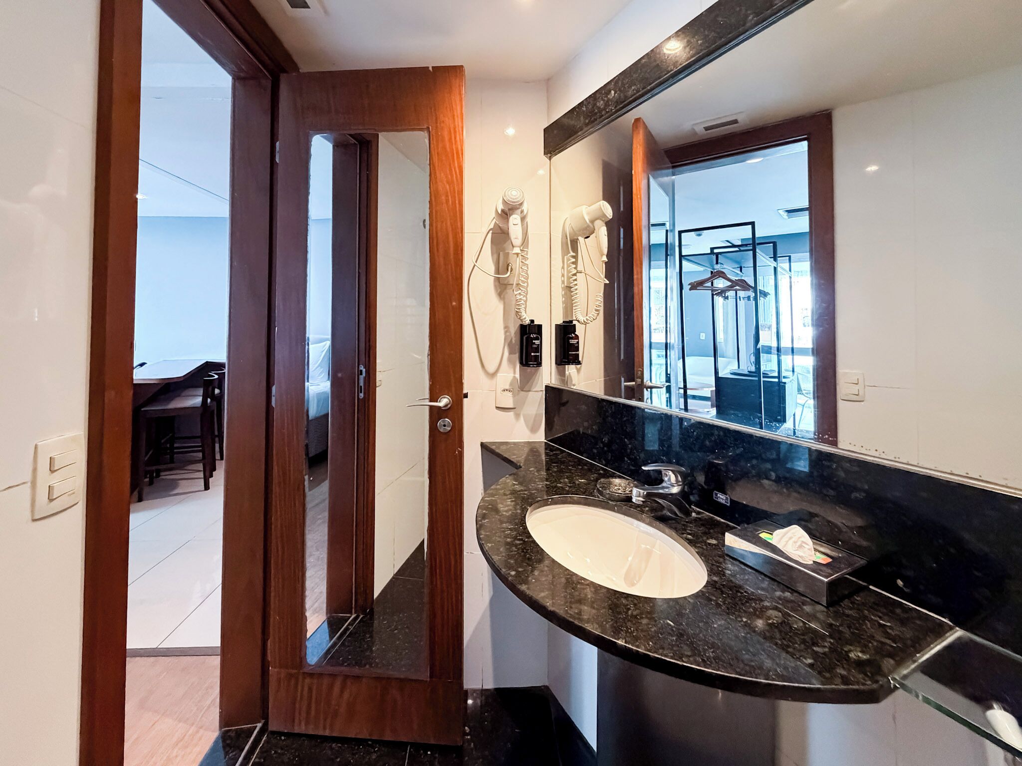 A modern bathroom with a large mirror, a sink, and hair dryers mounted on the wall.