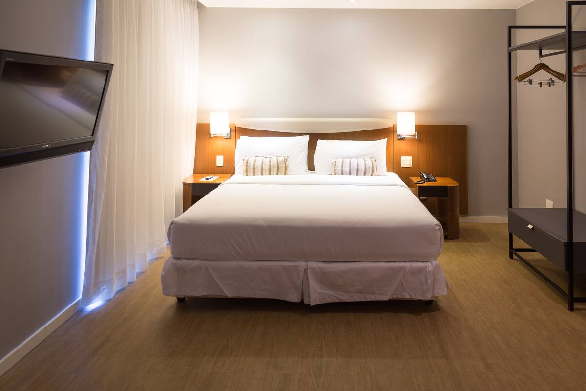 Ein Hotelzimmer mit einem großen Bett, Nachttischen, einem Fernseher und einem Kleiderschrank.