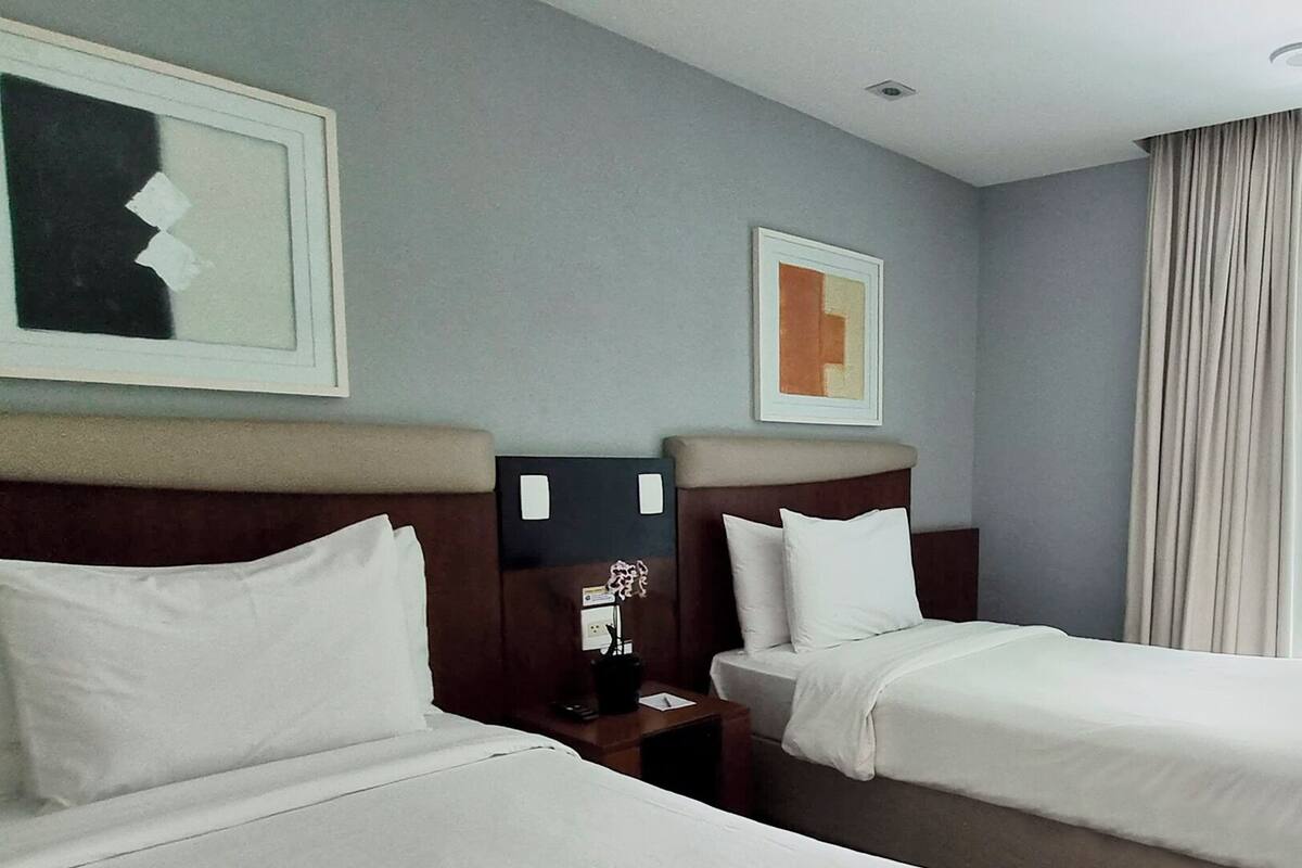 Ein Hotelzimmer mit zwei Betten, einem Nachttisch, einer Lampe und Bildern an den Wänden.