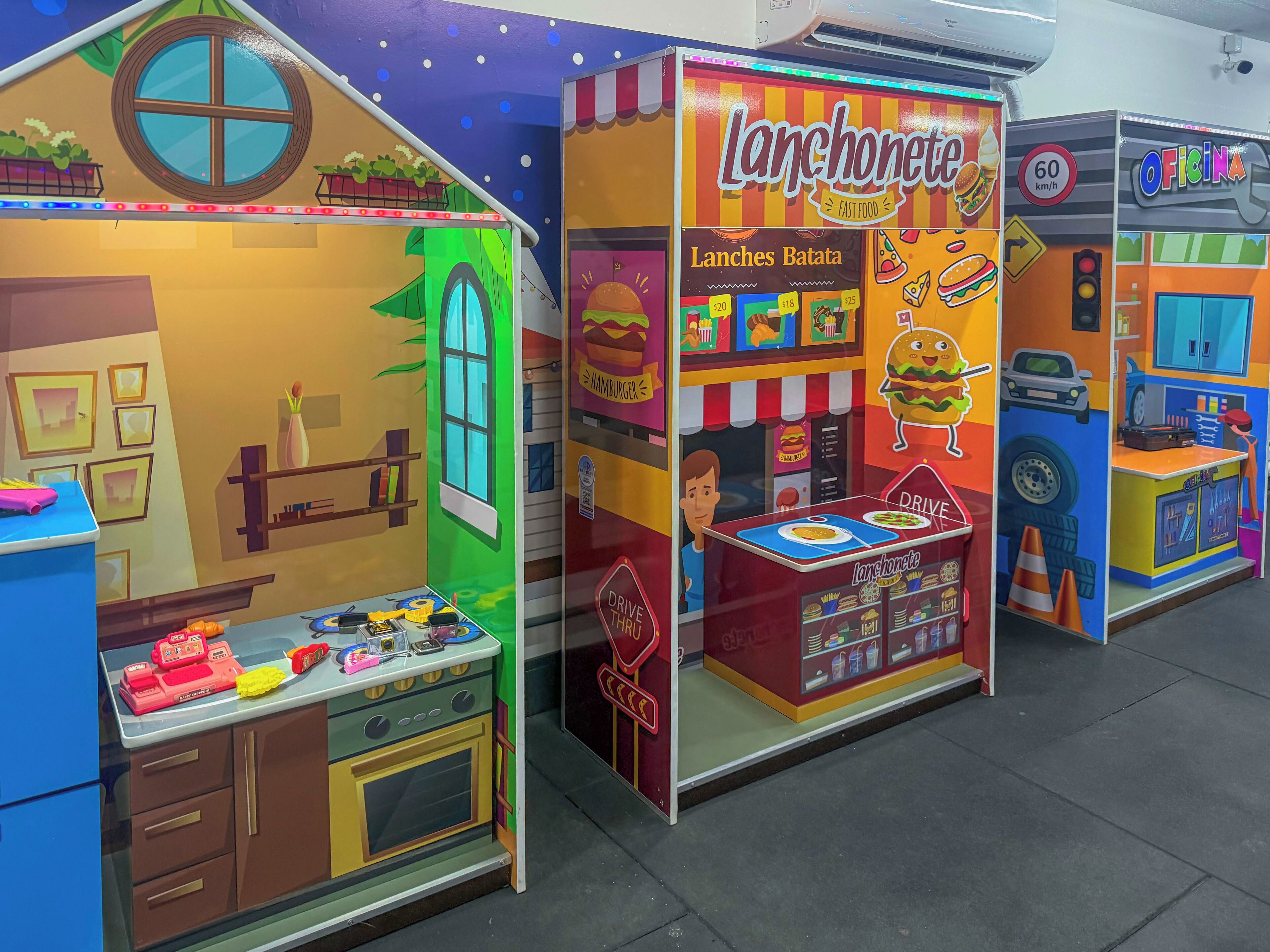 A colorful indoor play area with a 'Lanchonete' food stall, a 'Drive Thru' counter, and a 'Oficina' service area.