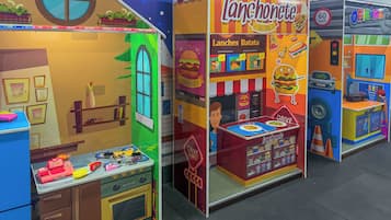 A colorful indoor play area with a 'Lanchonete' food stall, a 'Drive Thru' counter, and a 'Oficina' service area.