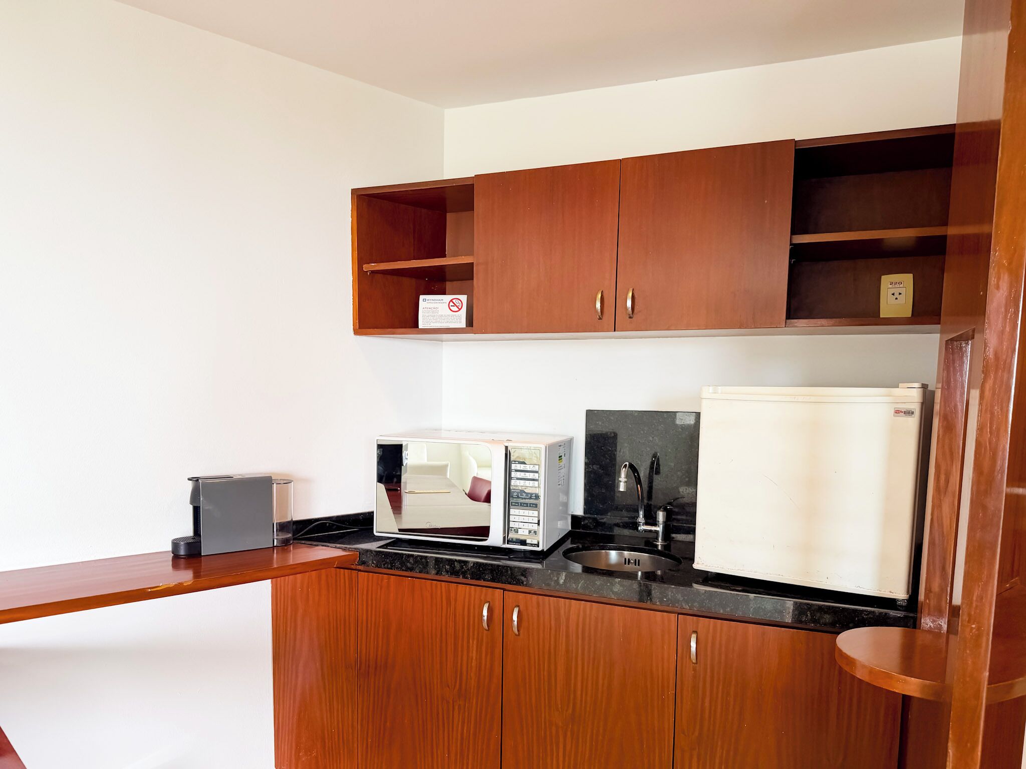 A compact kitchenette with wooden cabinets, a microwave, a coffee maker, and a sink.