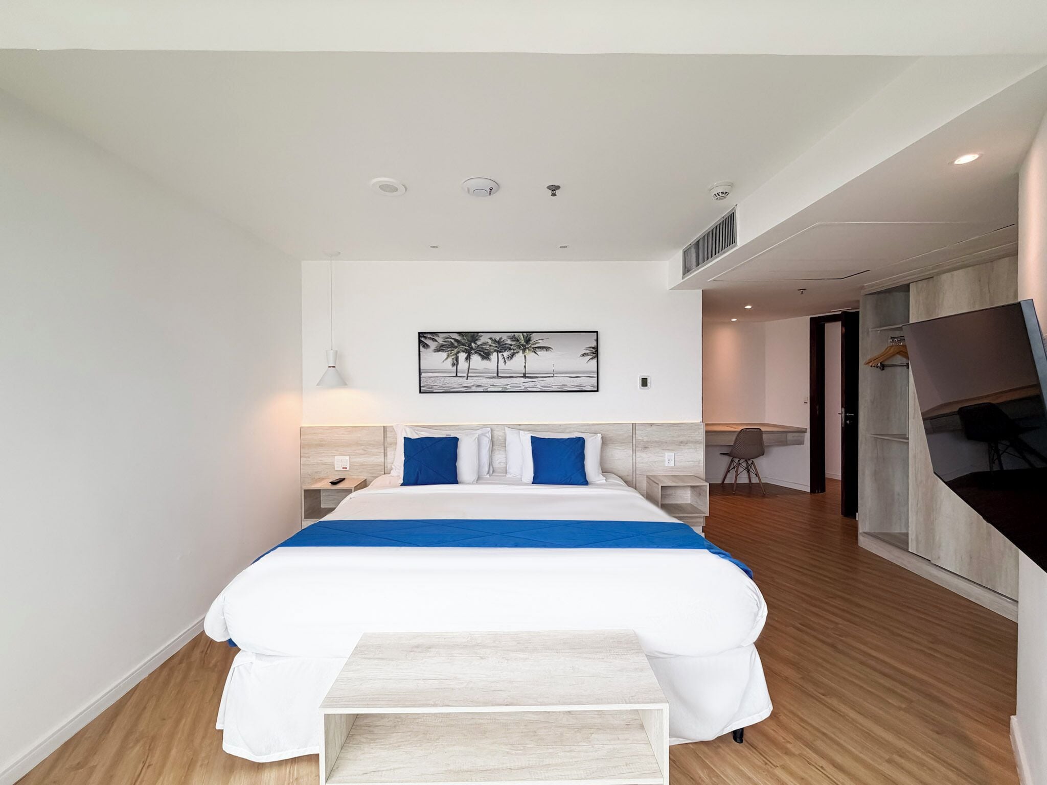A modern hotel room with a large bed, bedside tables, a desk, and a TV.