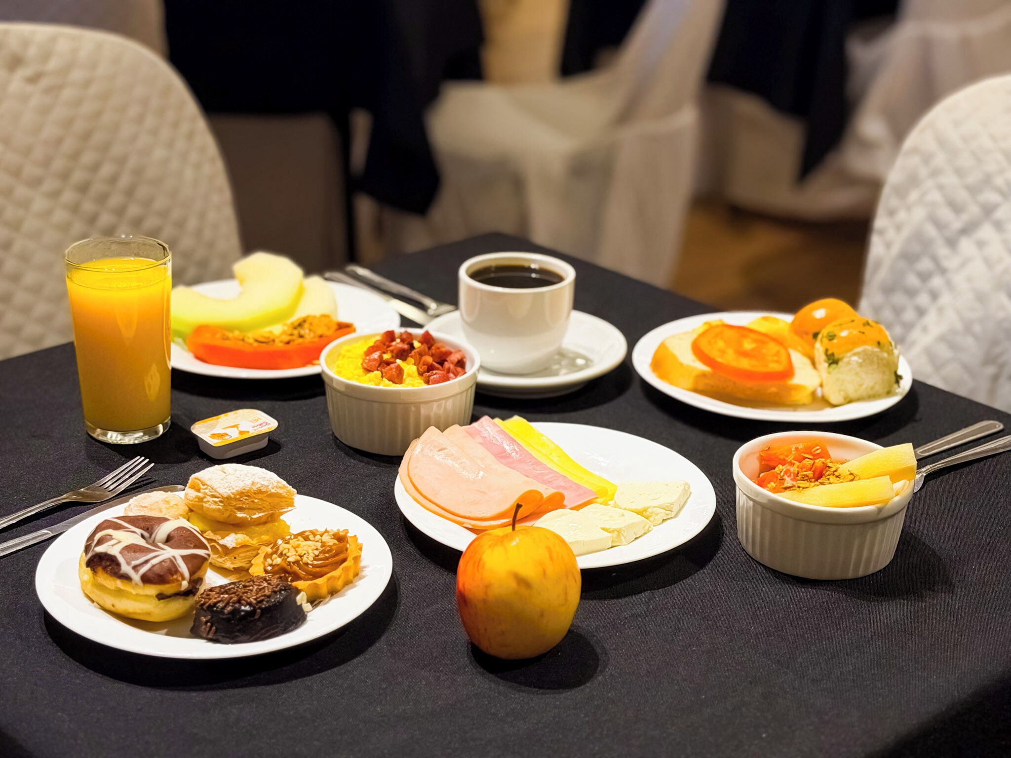 A breakfast table with various food items including eggs, ham, toast, fruit, and a glass of orange juice.