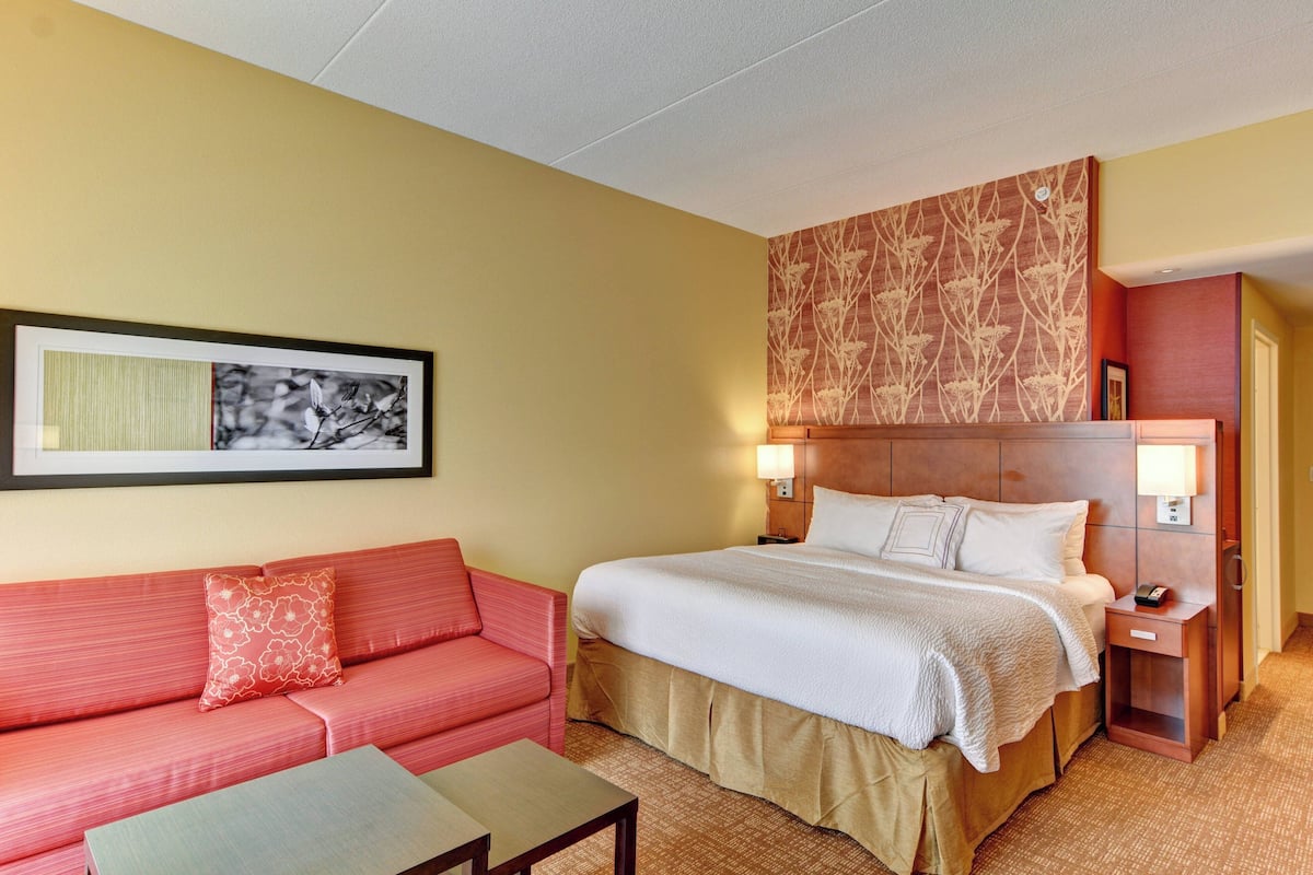 Una habitación de hotel con una cama, un sofá, una mesita y una lámpara en la mesita de noche.