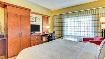 A hotel room with a large bed, a desk with a computer, a television, and a red chair.