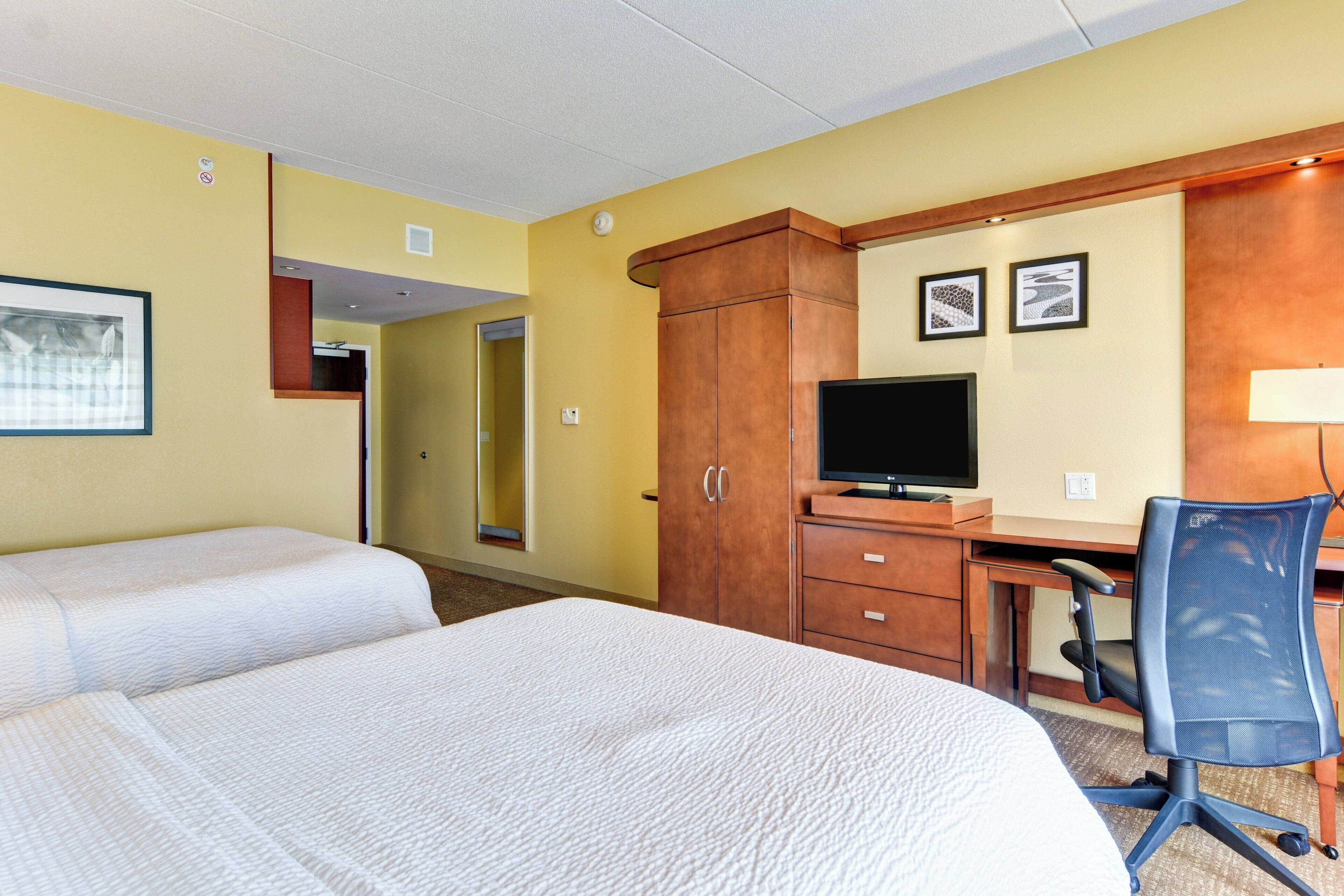 Une chambre d’hôtel avec deux lits, un bureau avec un ordinateur, une télévision et une chaise.