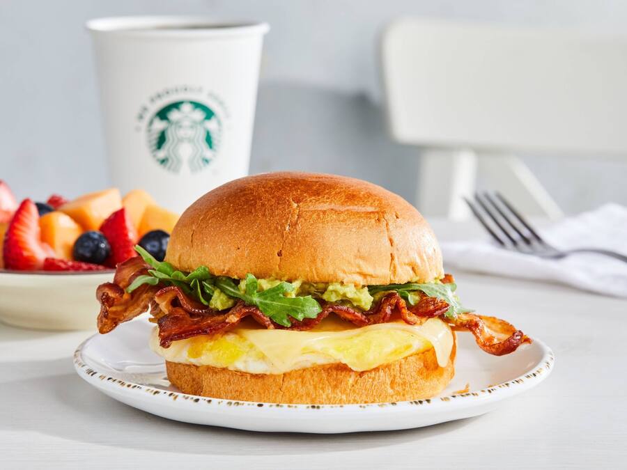 Ein Frühstückssandwich auf einem Teller, im Hintergrund eine Starbucks-Tasse.