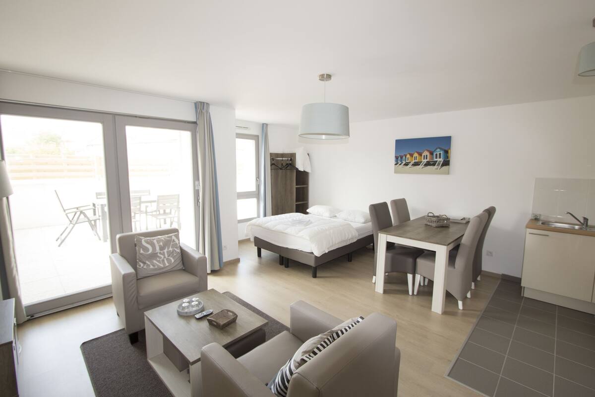 Una habitación de hotel moderna con cama, mesa de comedor, sofá y una pequeña cocina.